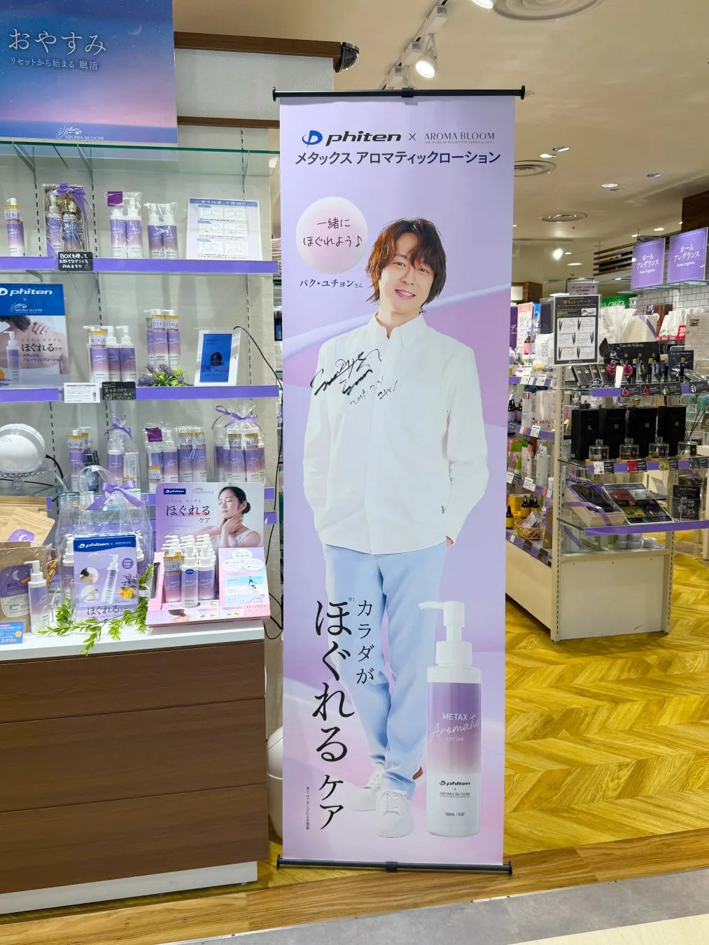 ファン必見!パク・ユチョン直筆サイン入り等身大バナーが当たる!AROMA BLOOMブラックフライデーで唯一無二のチャンス 3 店内にあるPhitenとAROMA BLOOMのコラボ商品の広告。モデルはパク・ユチョンさんで、メタックスアロマティックローションの宣伝をしている。商品は棚に並べられ、販促物も設置されている。