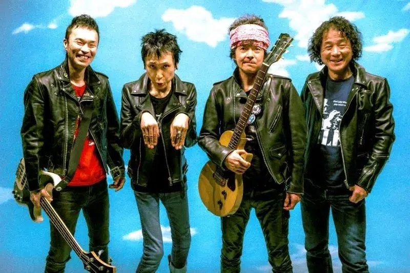 ロックバンドのメンバー4人のポートレート写真。全員が革ジャンを着ており、ギターやベースを持っている。背景は青空と雲のデザイン。
