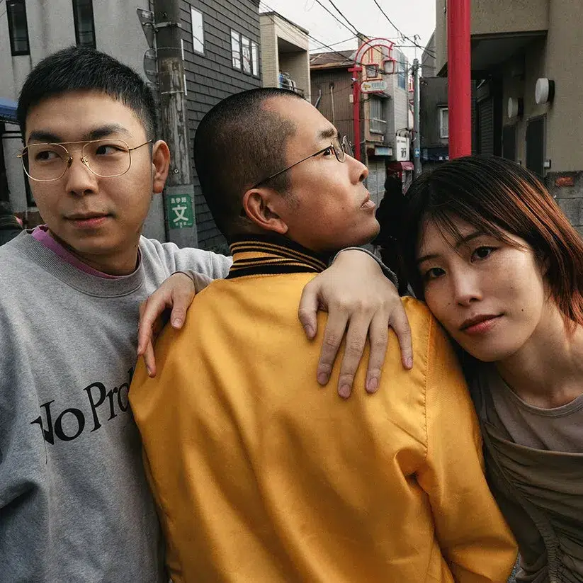 3人のアジア人が、街角で寄り添ってポーズをとっている写真