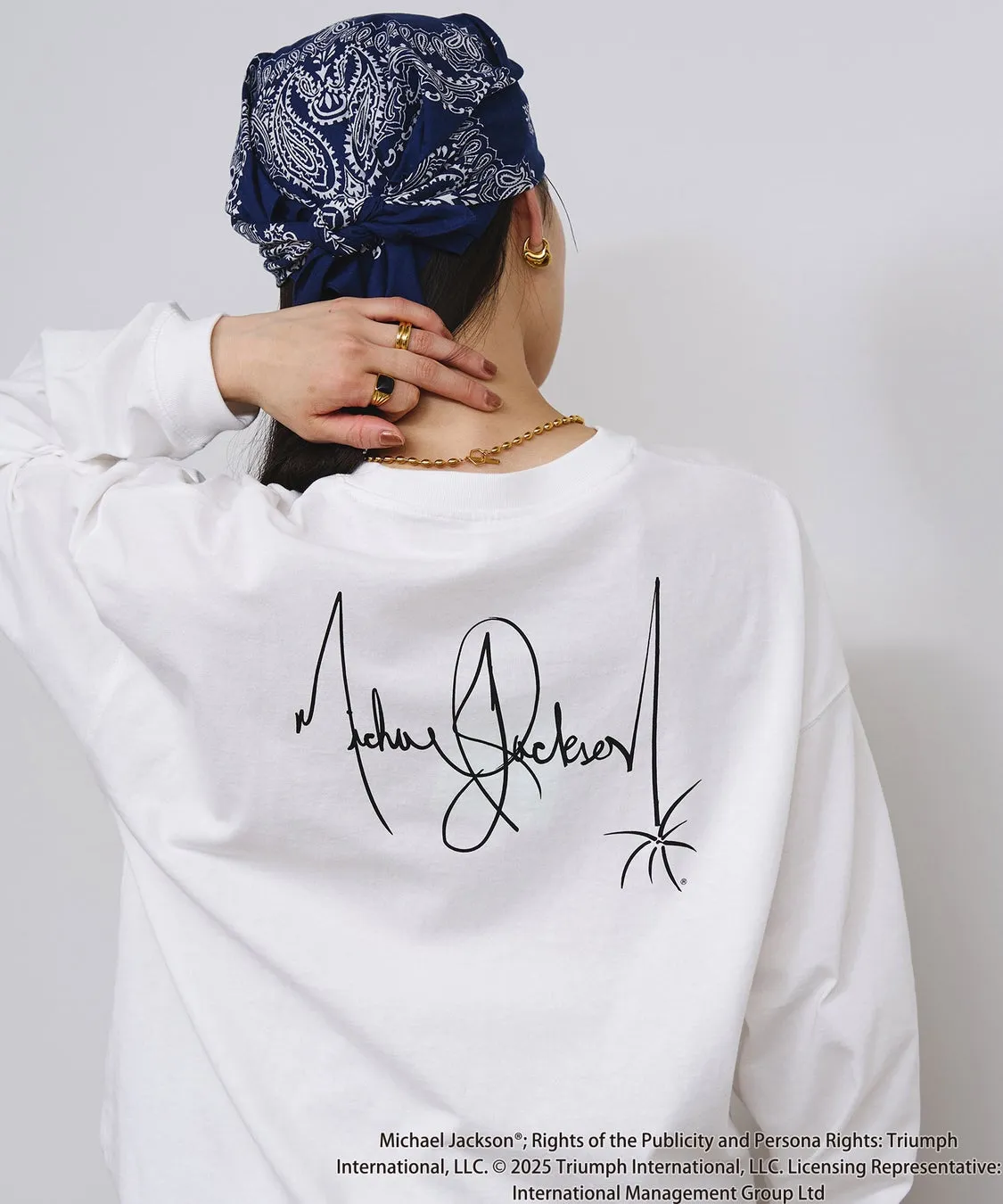 「KING OF POP」を纏う!ROSE BUDがマイケル・ジャクソン特別コレクションを初発表、ジェンダーレスで楽しめる全貌を公開! 11 後ろ姿の女性が、マイケル・ジャクソンのサインがプリントされた白い長袖Tシャツを着ています。