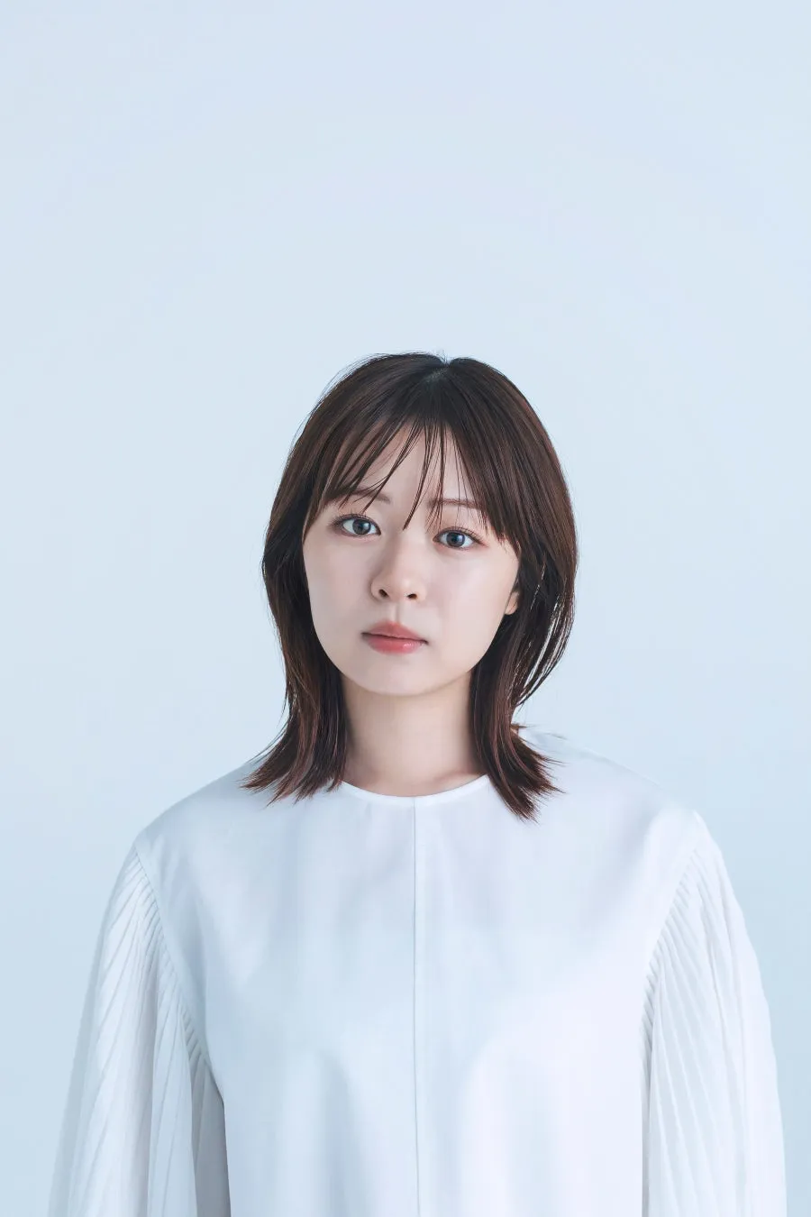 正面を向いた女性のポートレート。白いシャツを着ており、背景は白。