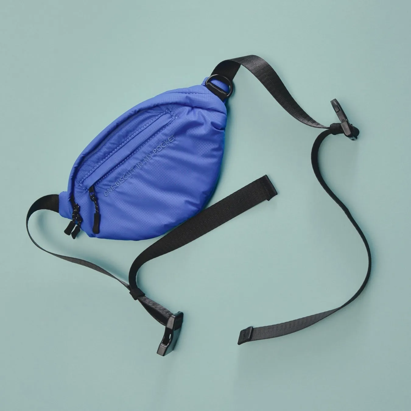 青色のウエストポーチが、水色の背景に置かれています。黒いストラップがポーチから伸びています。