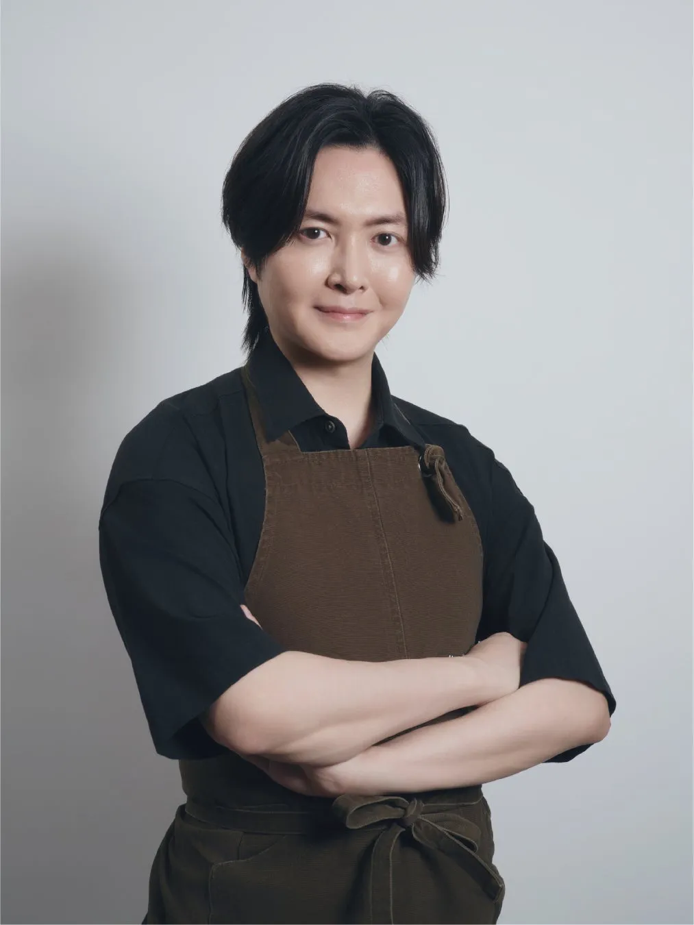 茶色のエプロンを着て腕を組んだ男性のポートレート。