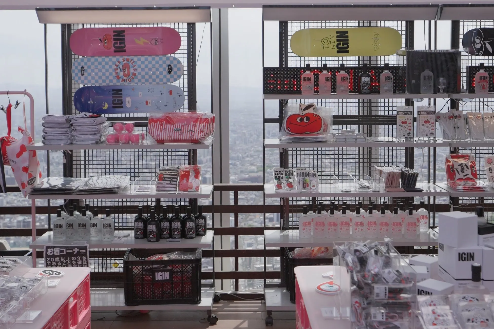 様々な商品が陳列された店の様子。スケートボード、酒瓶、バッグ、雑貨などが棚に並んでいる。店の奥には、窓から見える街並みが広がっている。