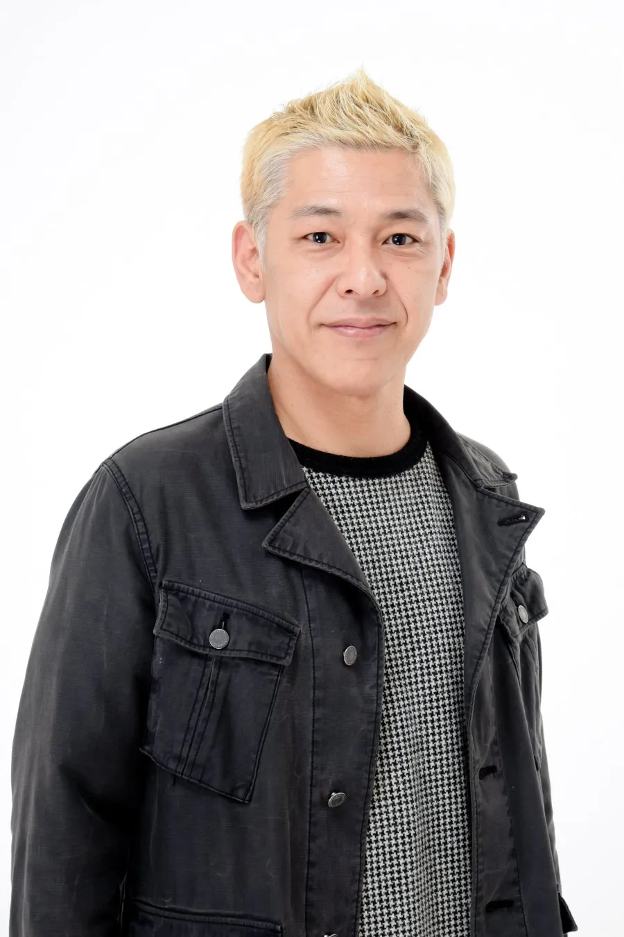 白髪交じりの髪型で、黒色のジャケットと千鳥格子のセーターを着た男性のポートレートです。