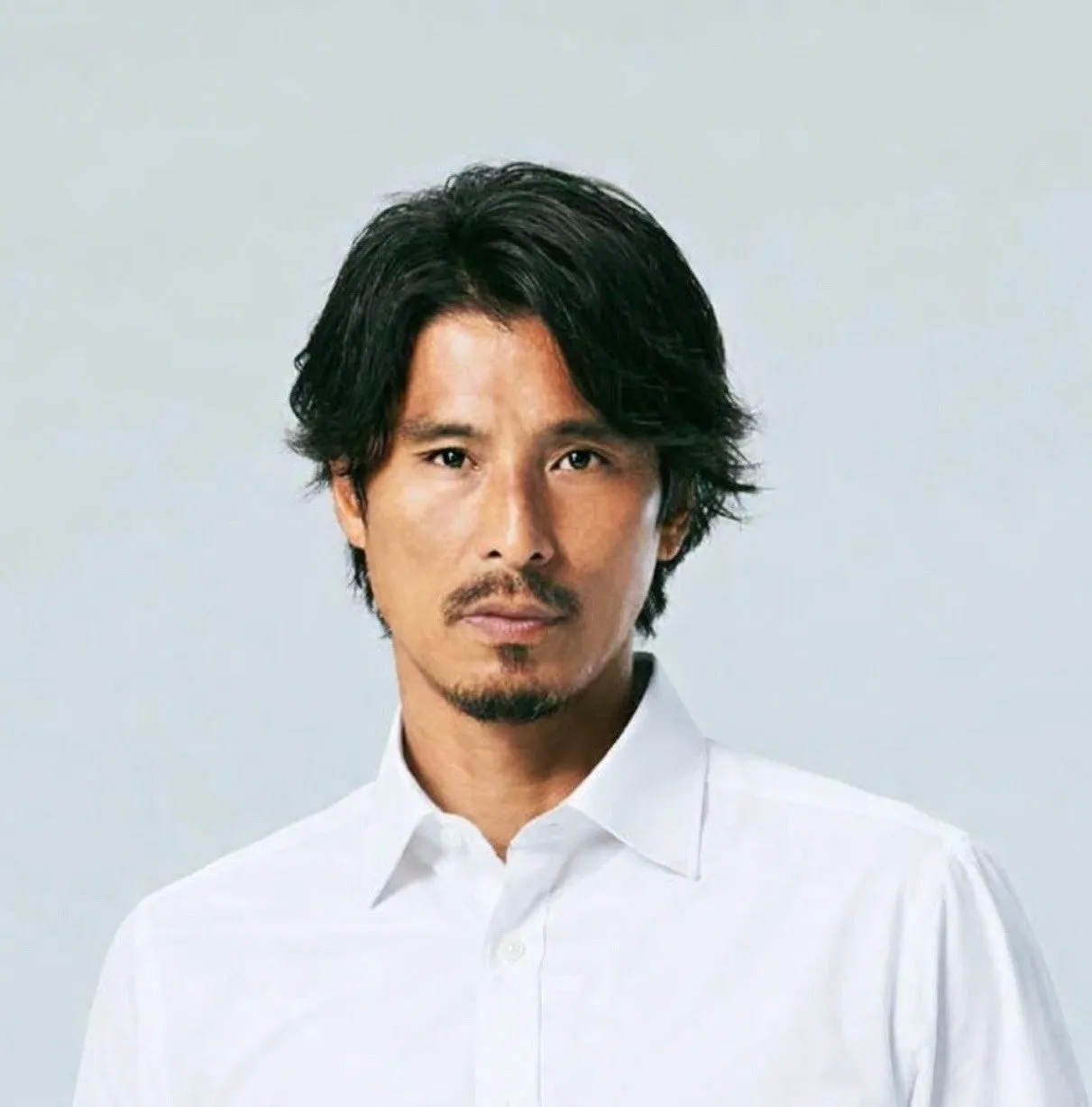 白いシャツを着た、アジア系の男性のポートレート。男性は少しのひげを生やし、黒い髪をしている。