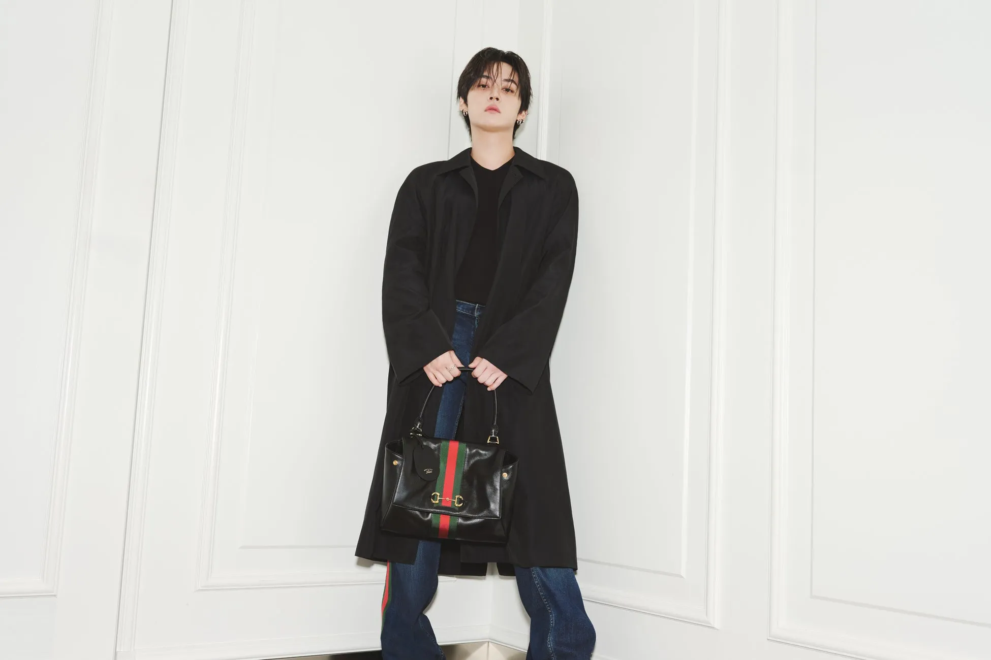Stray Kidsリノがグッチ「Generation Gucci」で魅せた新境地!唯一無二の洗練ルック2選を徹底解剖 3 黒のコートを着た男性が黒いハンドバッグを持った写真です。背景は白い壁です。